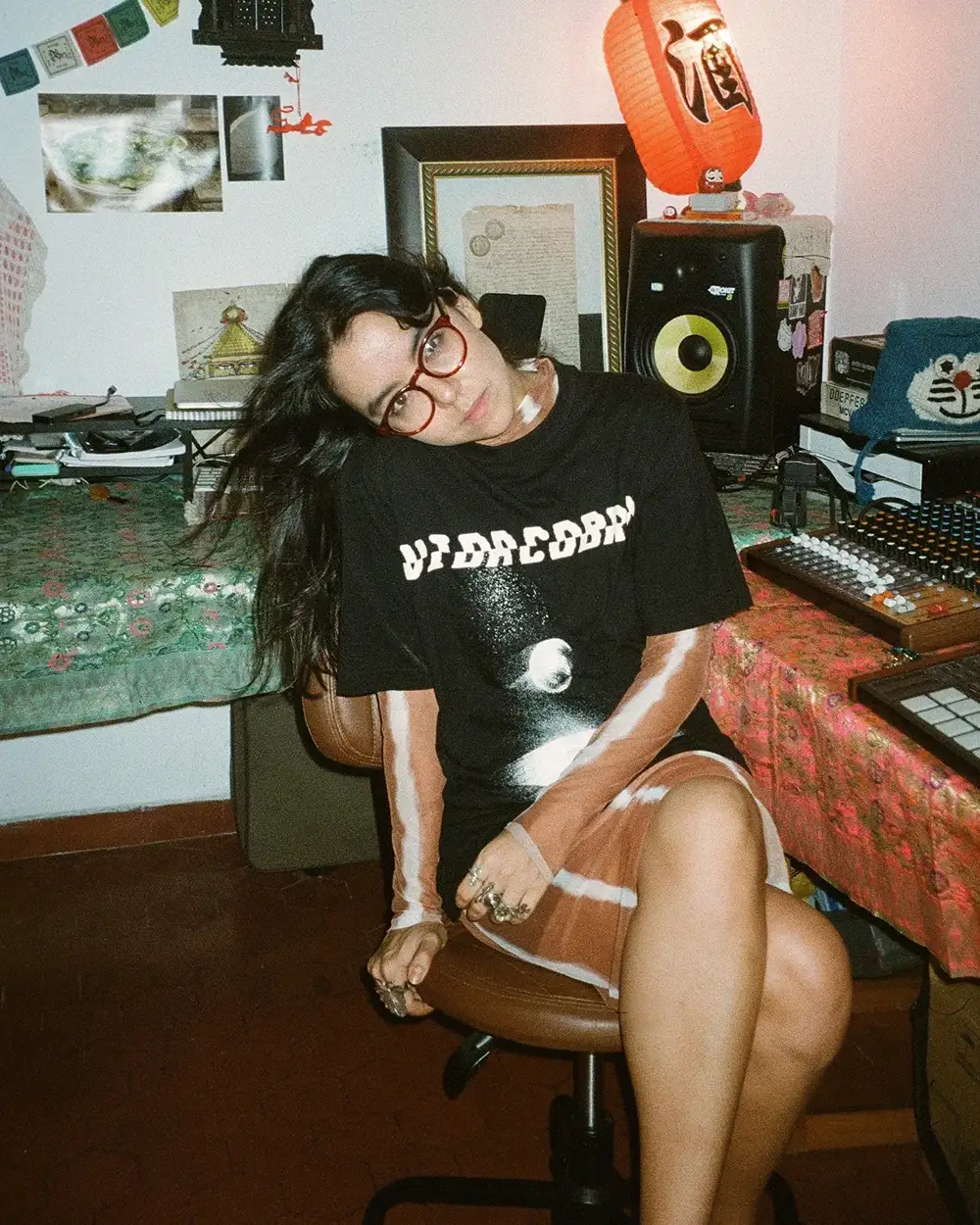 La DJ y productora chilena Valesuchi sentada en su estudio de producción musical en Santiago, rodeada de equipos electrónicos y decoraciones personales.