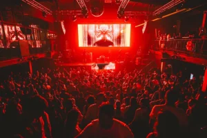 Vista panorámica del Club Chocolate en Santiago de Chile, lleno de público durante un concierto de música electrónica, con el escenario y la pista de baile iluminados en rojo intenso.