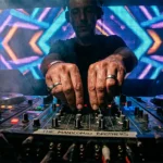 Primer plano de las manos de un DJ manipulando la mezcladora en una cabina oscura, guiando el viaje musical en fiesta de santiago de chile