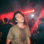 Un raver con ojos cerrados experimentando inmersión total bajo luces rojas en un club de techno underground en Santiago.