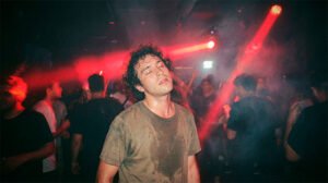 Un raver con ojos cerrados experimentando inmersión total bajo luces rojas en un club de techno underground en Santiago.